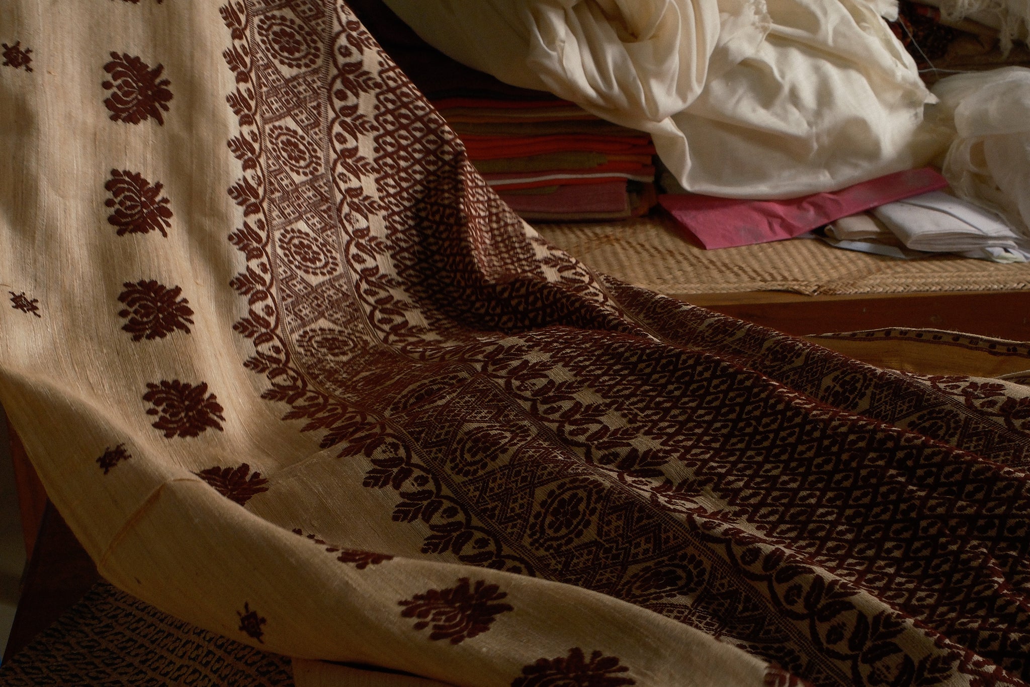 Textile with intricate patterns on a bed with books and clothes in the background